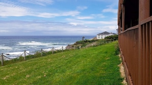A coastal view with a grassy slope, a wooden fence, and a building in the background.