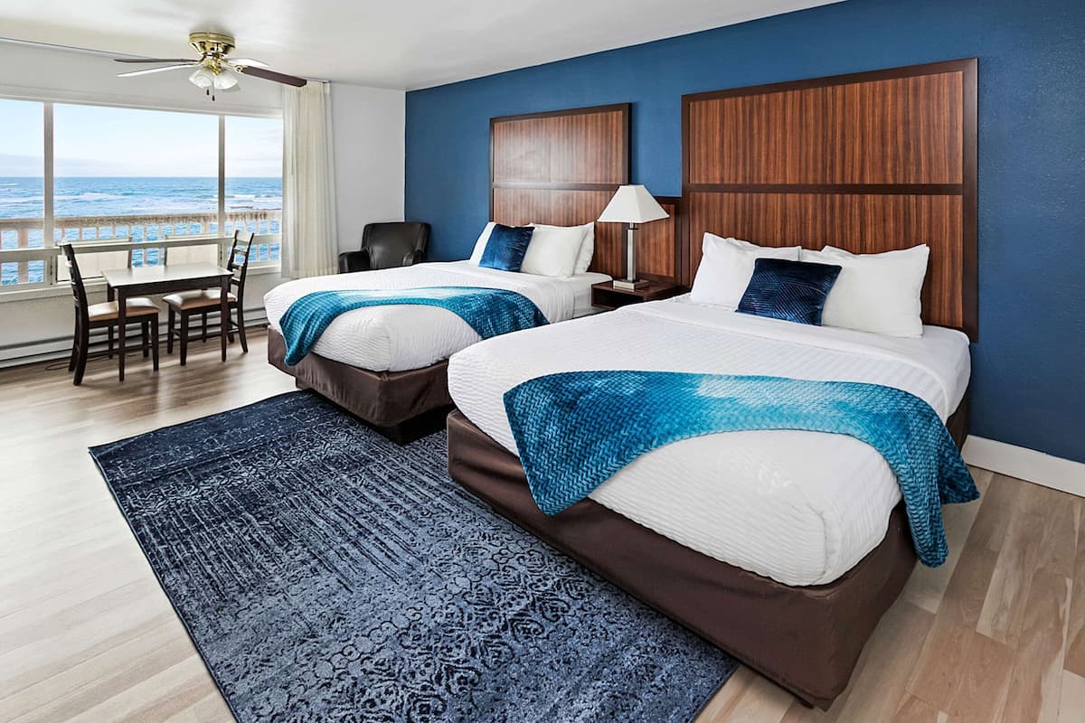 Une chambre d’hôtel avec deux lits, un bureau et une chaise. La chambre dispose d’une grande fenêtre donnant sur l’océan.