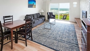 A modern living room with a dining area, a sofa, a coffee table, and a view of the ocean through large glass doors.
