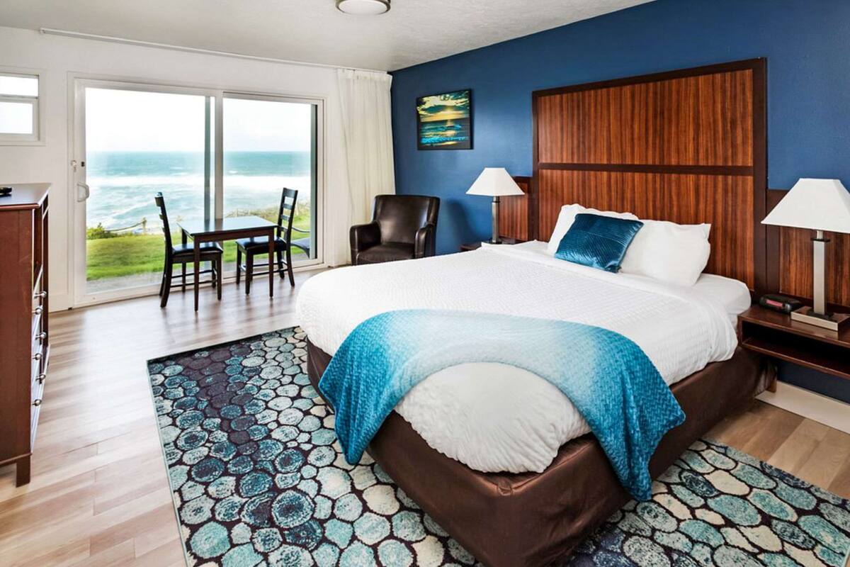 Une chambre d’hôtel avec un grand lit, une vue sur l’océan, une tête de lit en bois et un bureau avec une chaise.