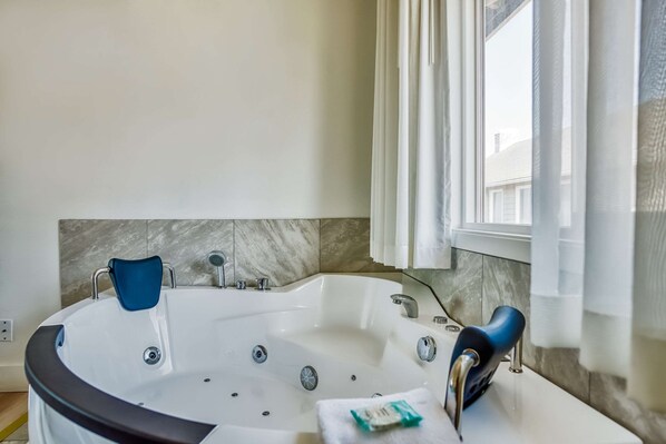 A modern bathroom with a freestanding bathtub, marble tiles, and a window with curtains.