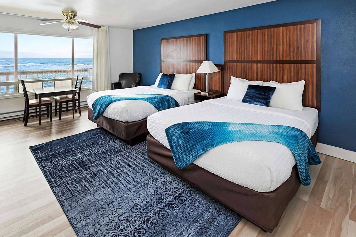 Une chambre d’hôtel avec deux lits, un bureau, une chaise, une lampe et une vue sur l’océan.