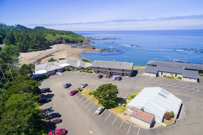 An aerial view of a parking lot with several cars, a building with a flat roof, and a beach in the background.