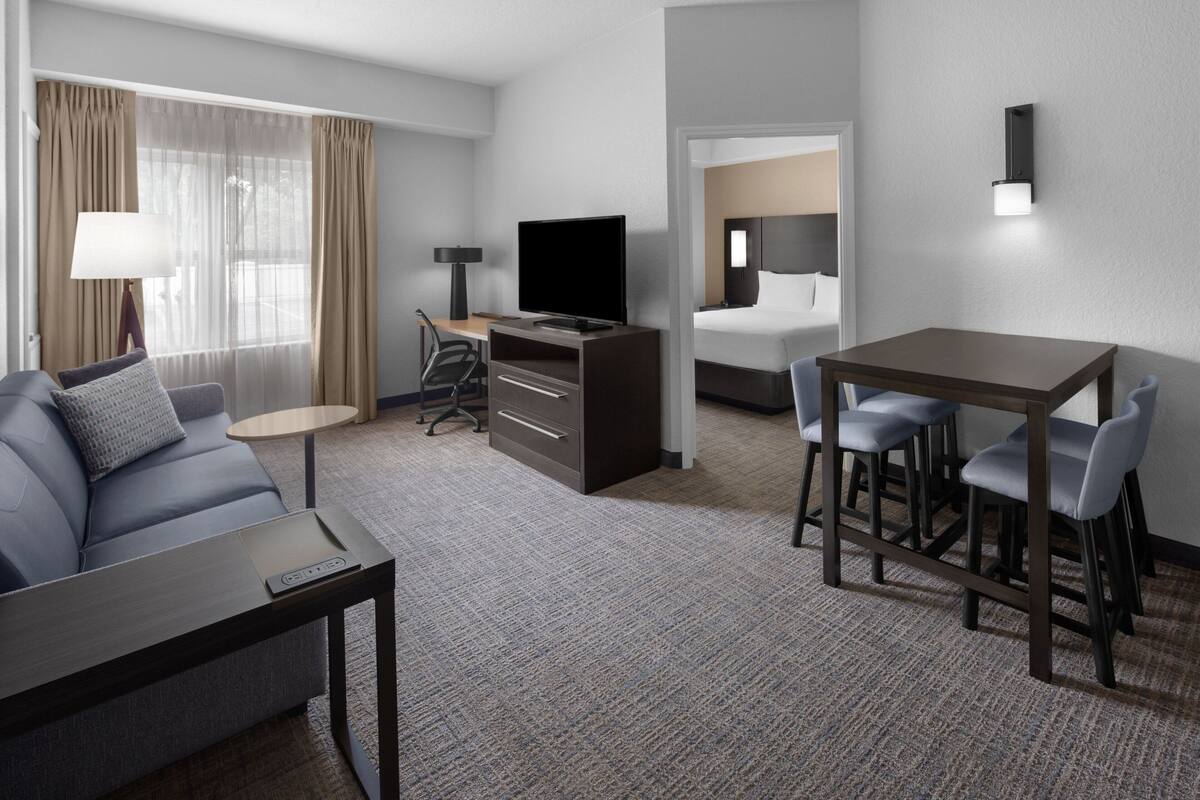 Une chambre d’hôtel comprenant un canapé, un bureau avec un ordinateur, une télévision, un lit et un petit coin repas.