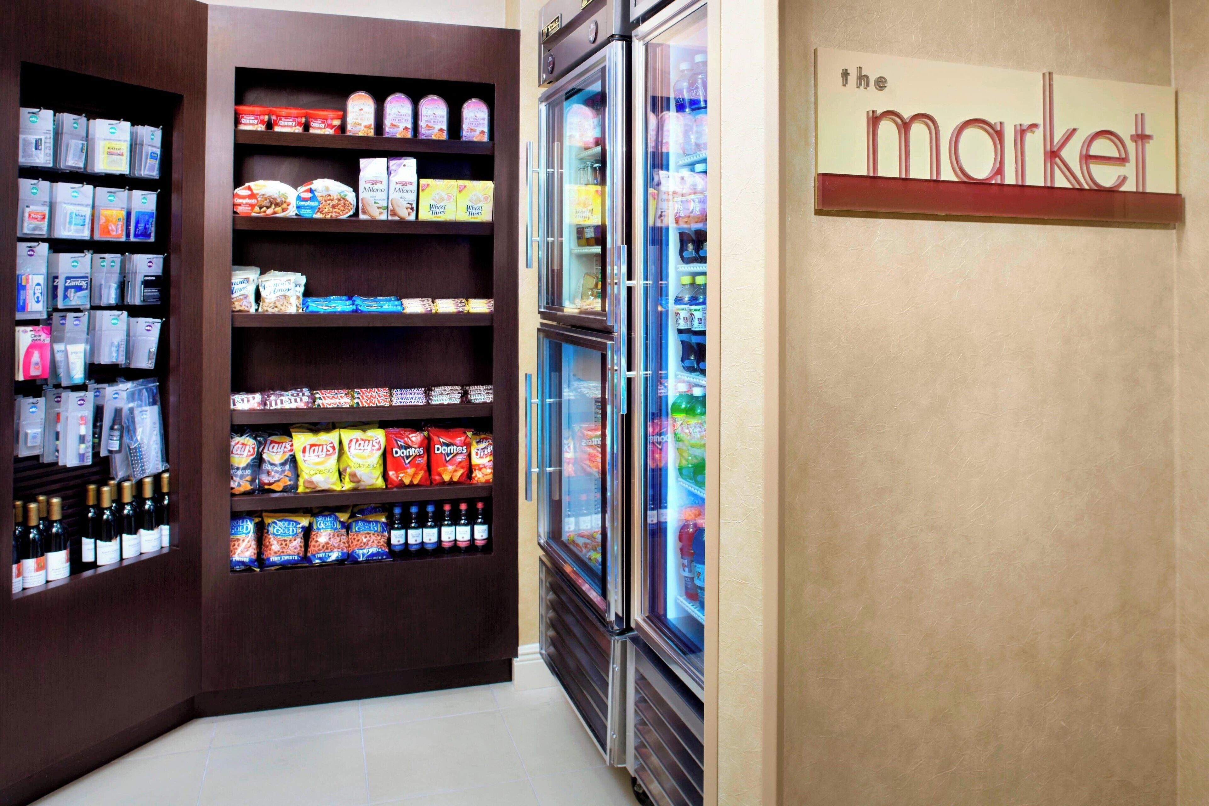 Interior de un supermercado con estantes llenos de aperitivos, bebidas y productos refrigerados.