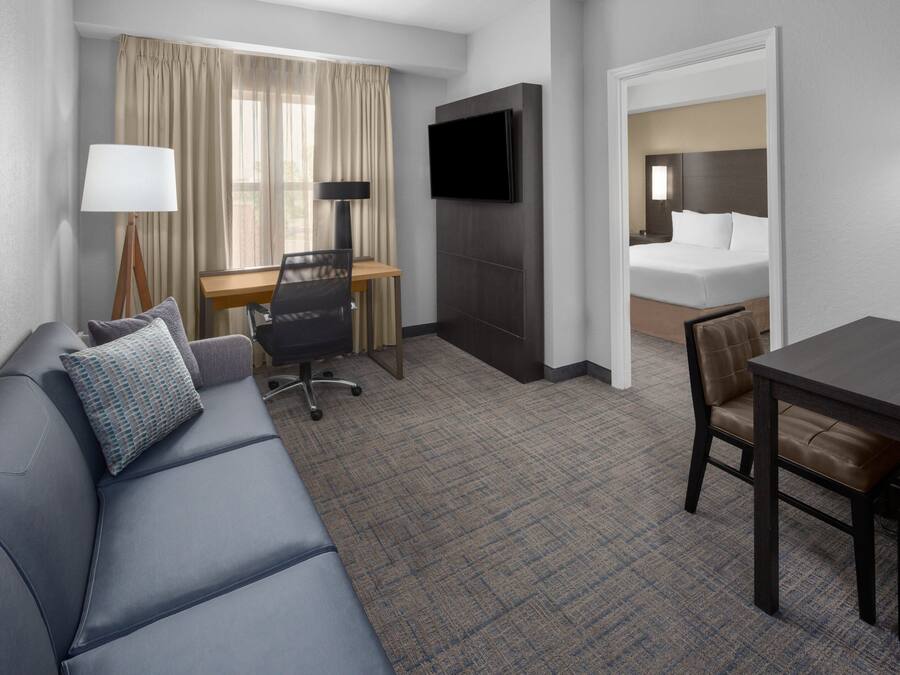 Een hotelkamer met een bank, een bureau, een televisie, een bed en een eettafel.