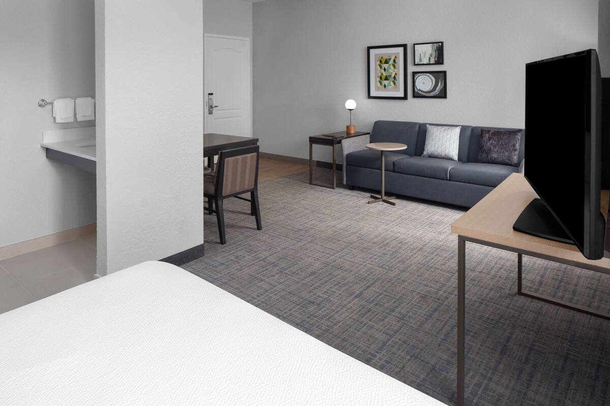 Une chambre d’hôtel avec un lit, un bureau, un canapé, une télévision et une petite table avec une lampe.