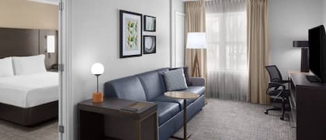 A hotel room with a bed, a sofa, a desk, a chair, and a TV.
