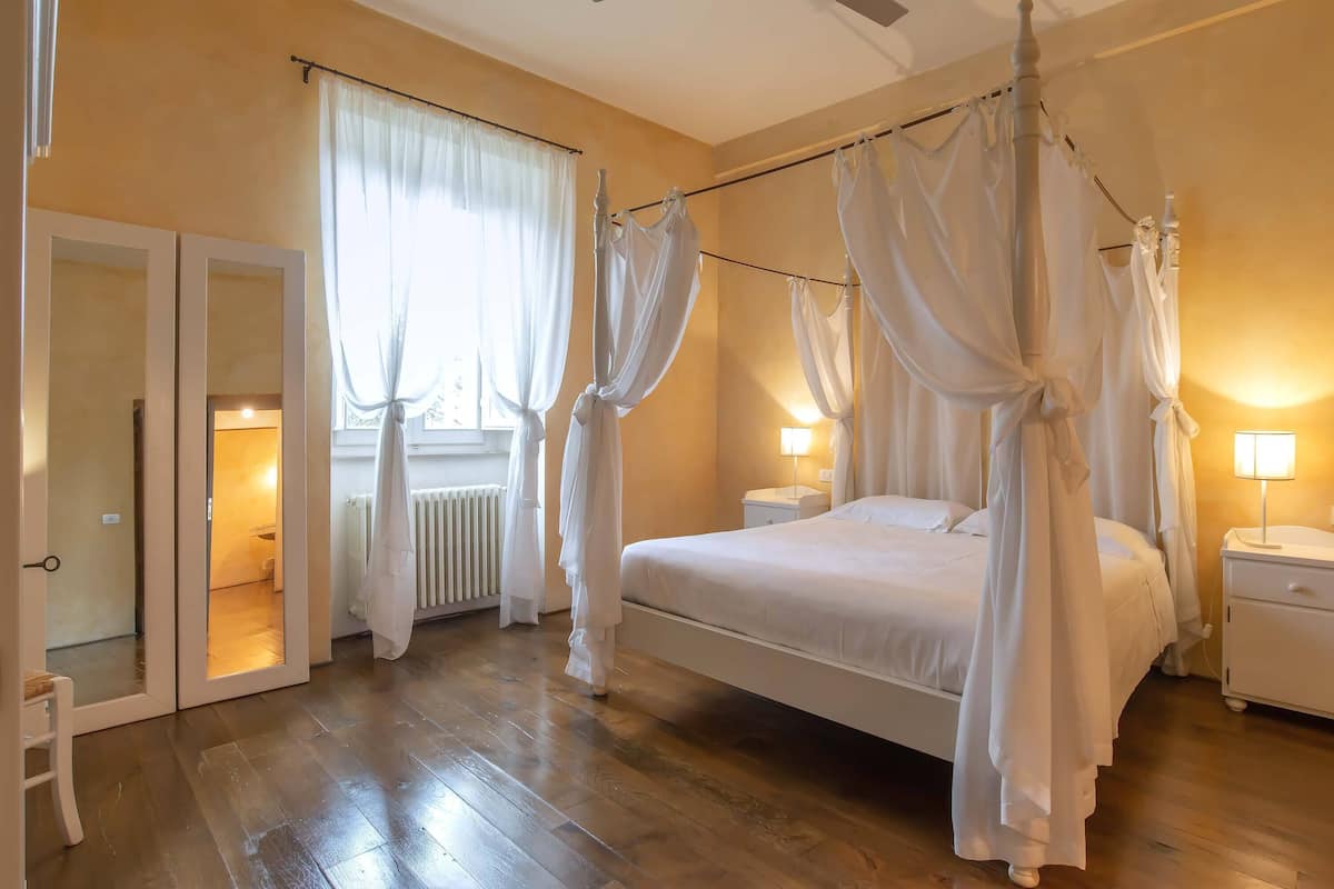 Ein Schlafzimmer mit einem Himmelbett, einem Nachttisch, einer Lampe und Blick auf ein Badezimmer durch eine offene Tür.