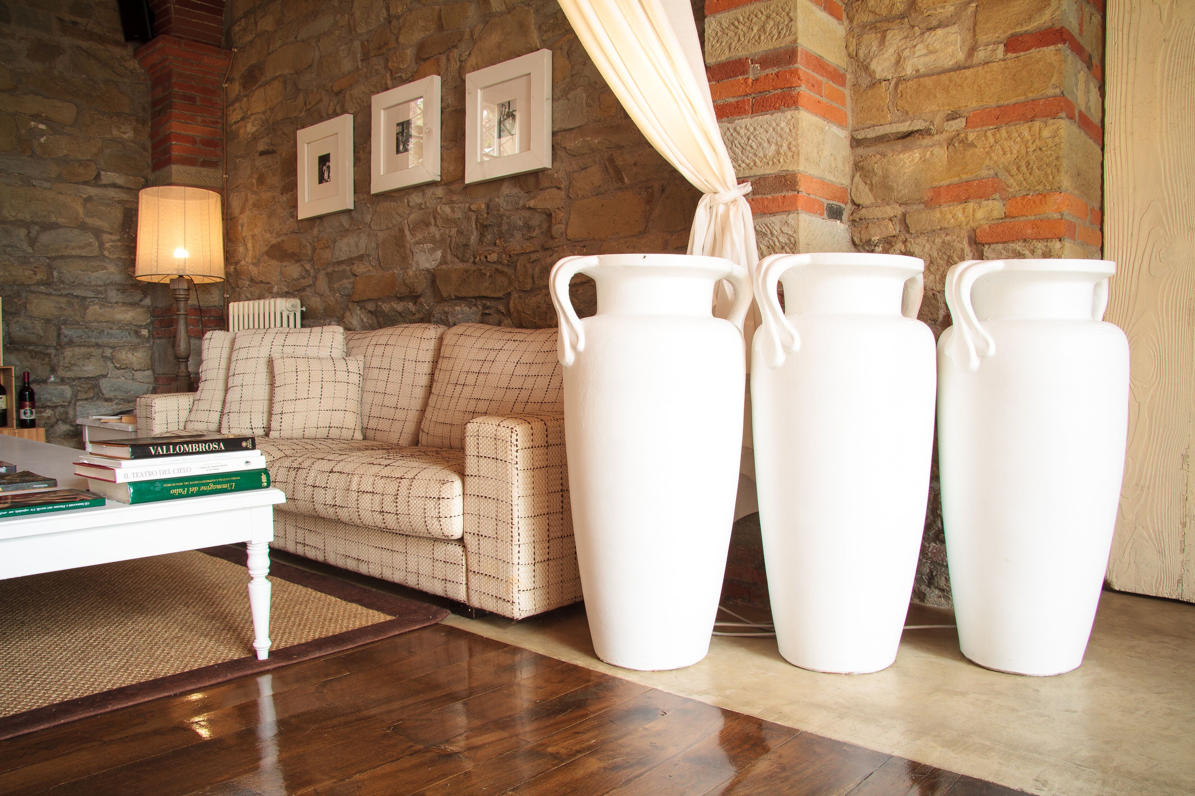 A living room with a stone wall, a patterned sofa, a white coffee table with books, and three white vases.