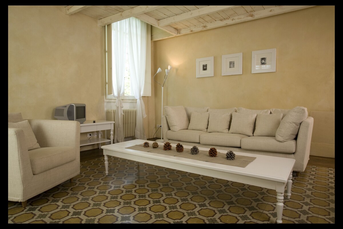A living room with a sofa, armchair, coffee table, and a radiator. There are pine cones on the coffee table and a lamp beside the sofa.