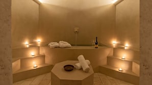 Een spa-ruimte met een badkuip, kaarsen, handdoeken en een fles wijn.