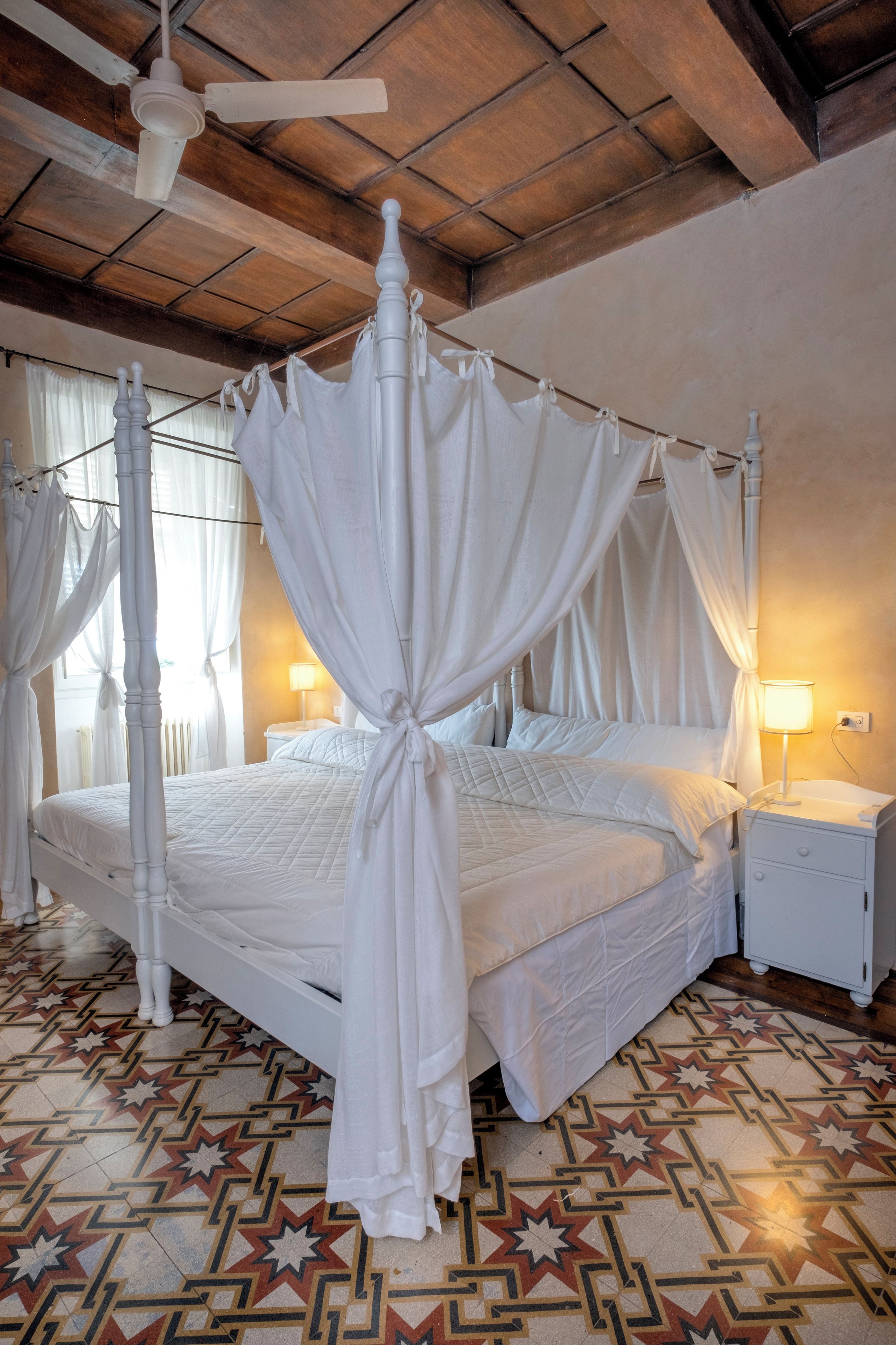 A four-poster canopy bed with a white canopy, a wooden ceiling, and a patterned floor.