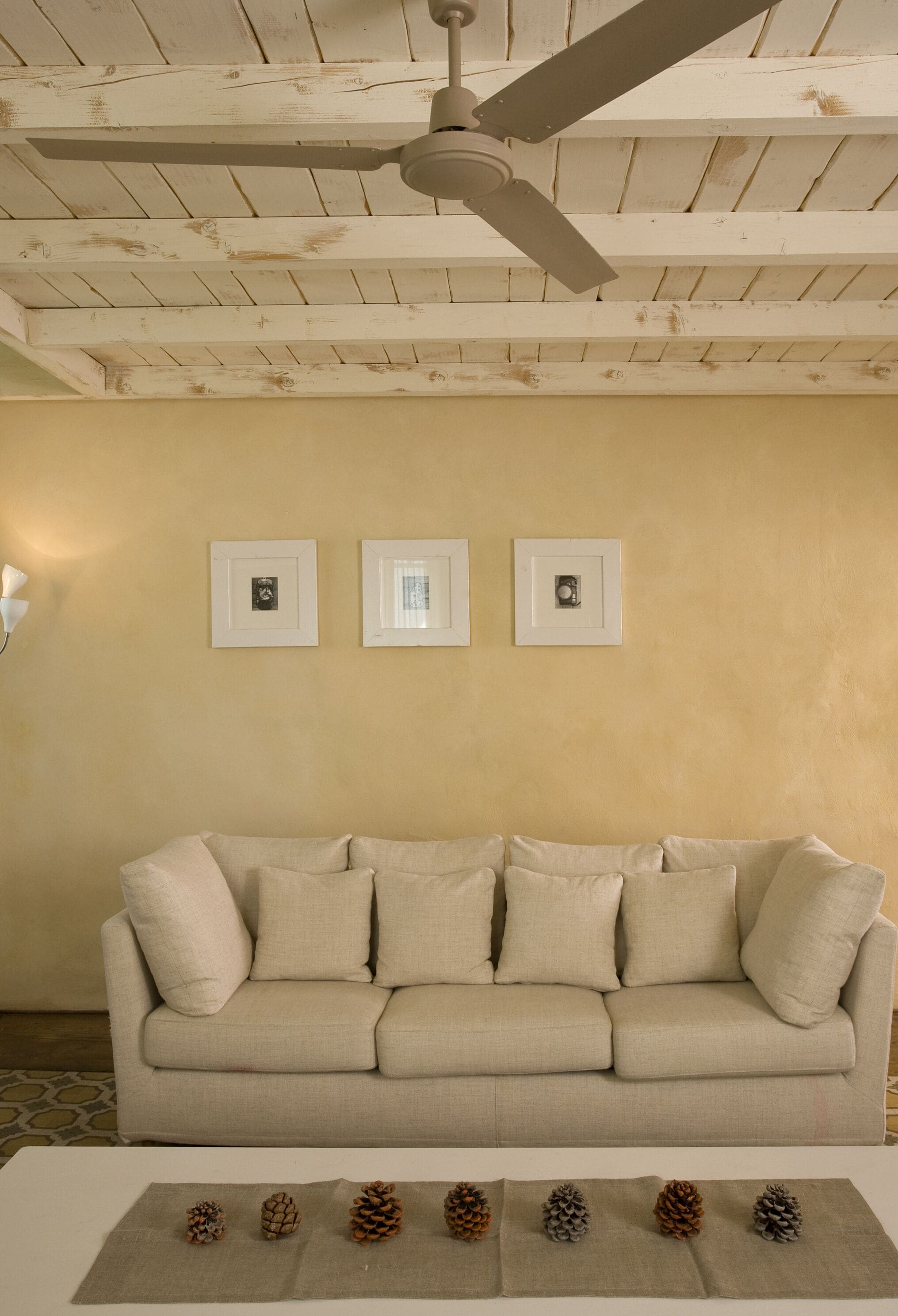 A room with a ceiling fan, a beige couch, and three framed pictures on the wall.