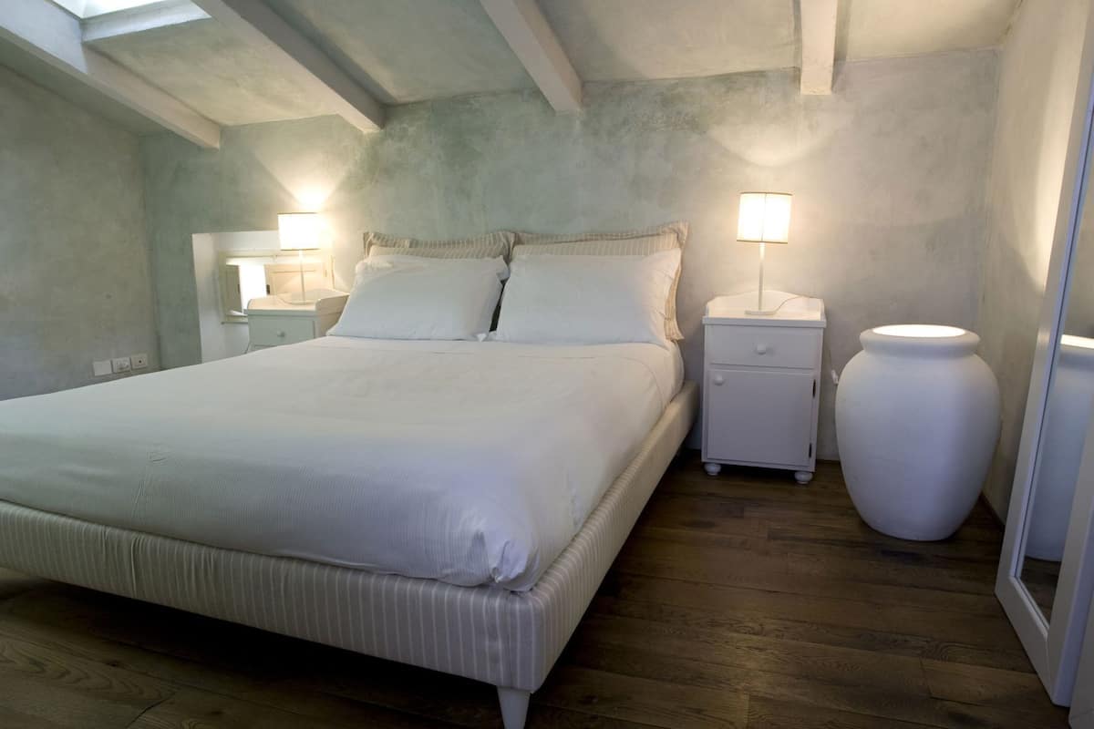Ein Schlafzimmer mit einem großen Bett, zwei Nachttischen mit Lampen, einem Beistelltisch und einer großen Vase.