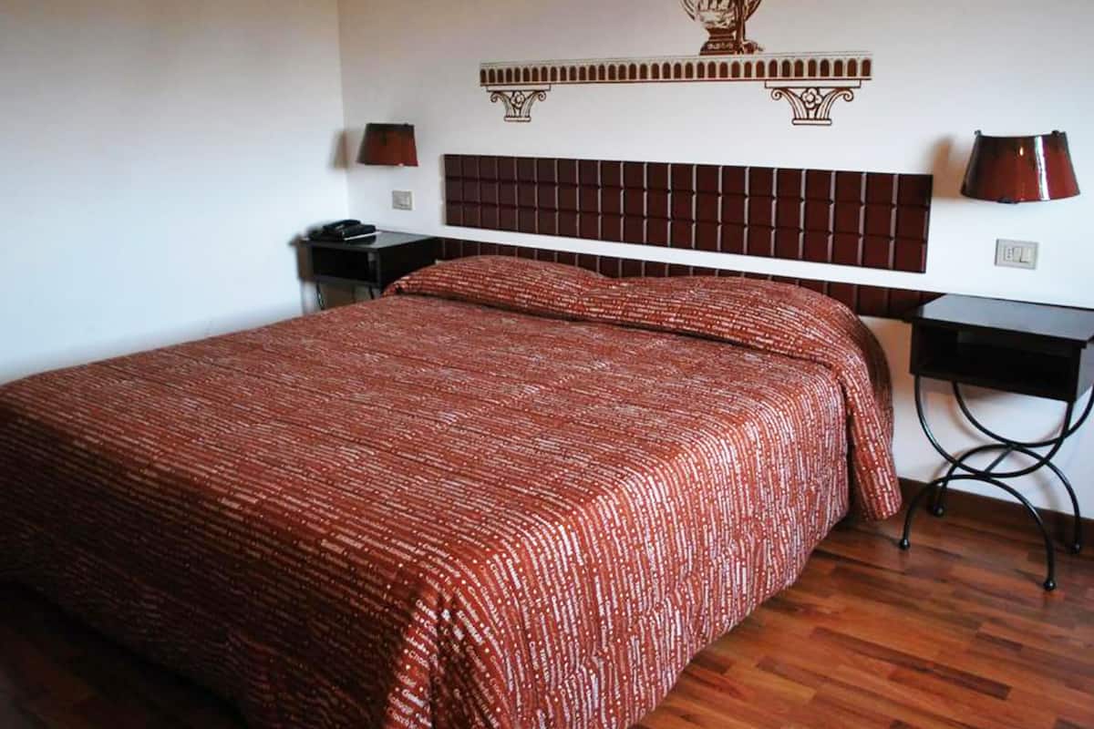 Une chambre d’hôtel avec un grand lit, deux tables de chevet, un élément décoratif mural au-dessus du lit et une petite table de chevet avec une lampe.