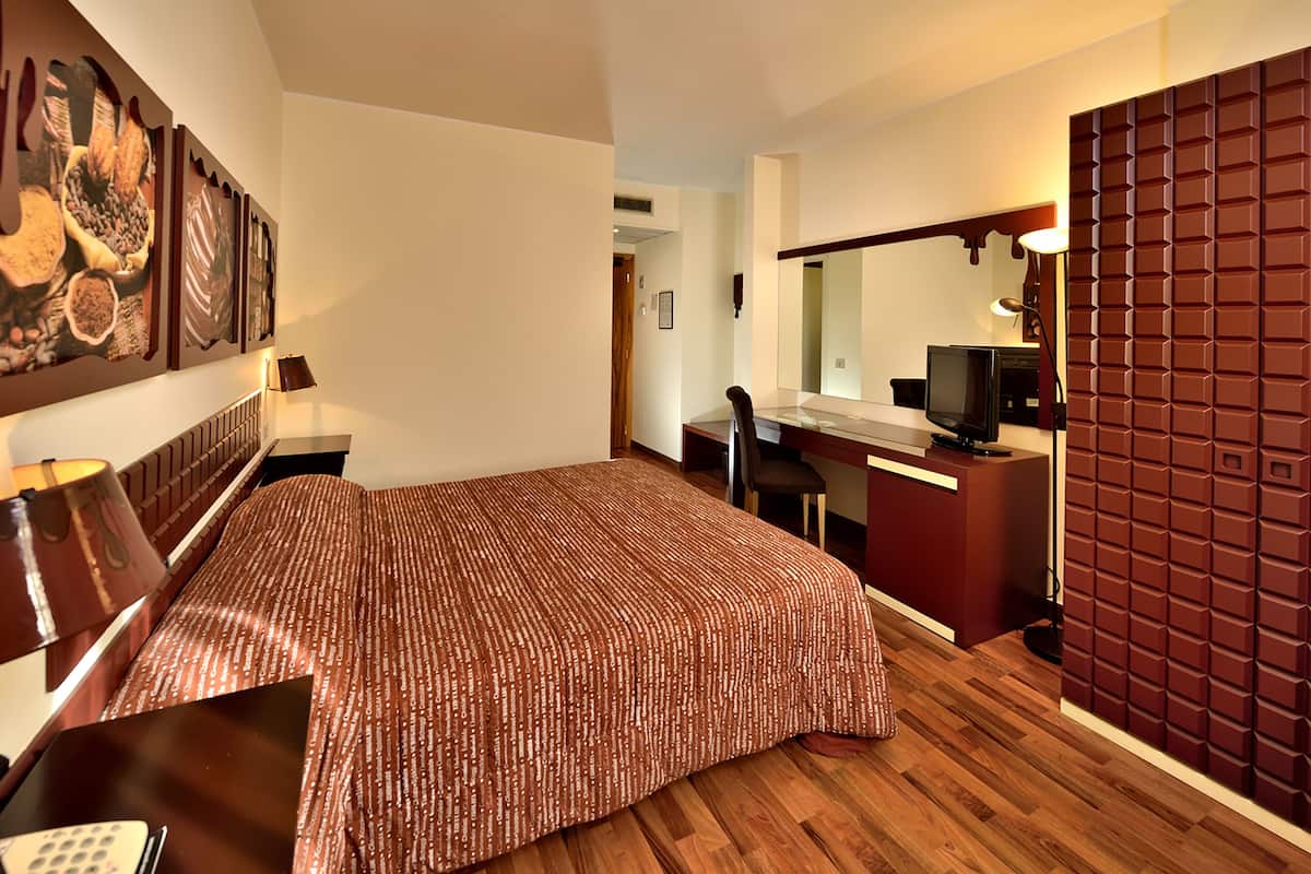 Une chambre d’hôtel avec un lit, un bureau, une chaise, une télévision et un grand miroir.