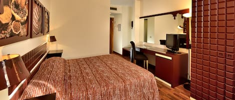 A hotel room with a bed, a desk, a chair, a television, and a large mirror.
