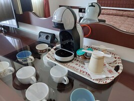 Una estación de café con una cafetera, tazas y una bandeja con cápsulas de café.