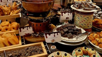 Un bufé con diversos postres, entre ellos opciones bañadas en chocolate, pastelería y una cascada de chocolate.