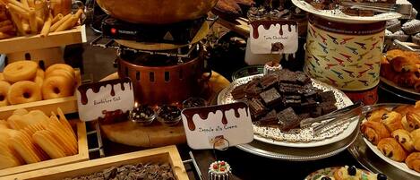 Un bufé con diversos postres, entre ellos opciones bañadas en chocolate, pastelería y una cascada de chocolate.
