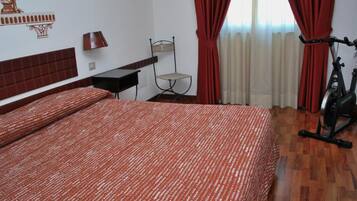 A hotel room with a large bed, a chair, a desk, a lamp, and an exercise bike.