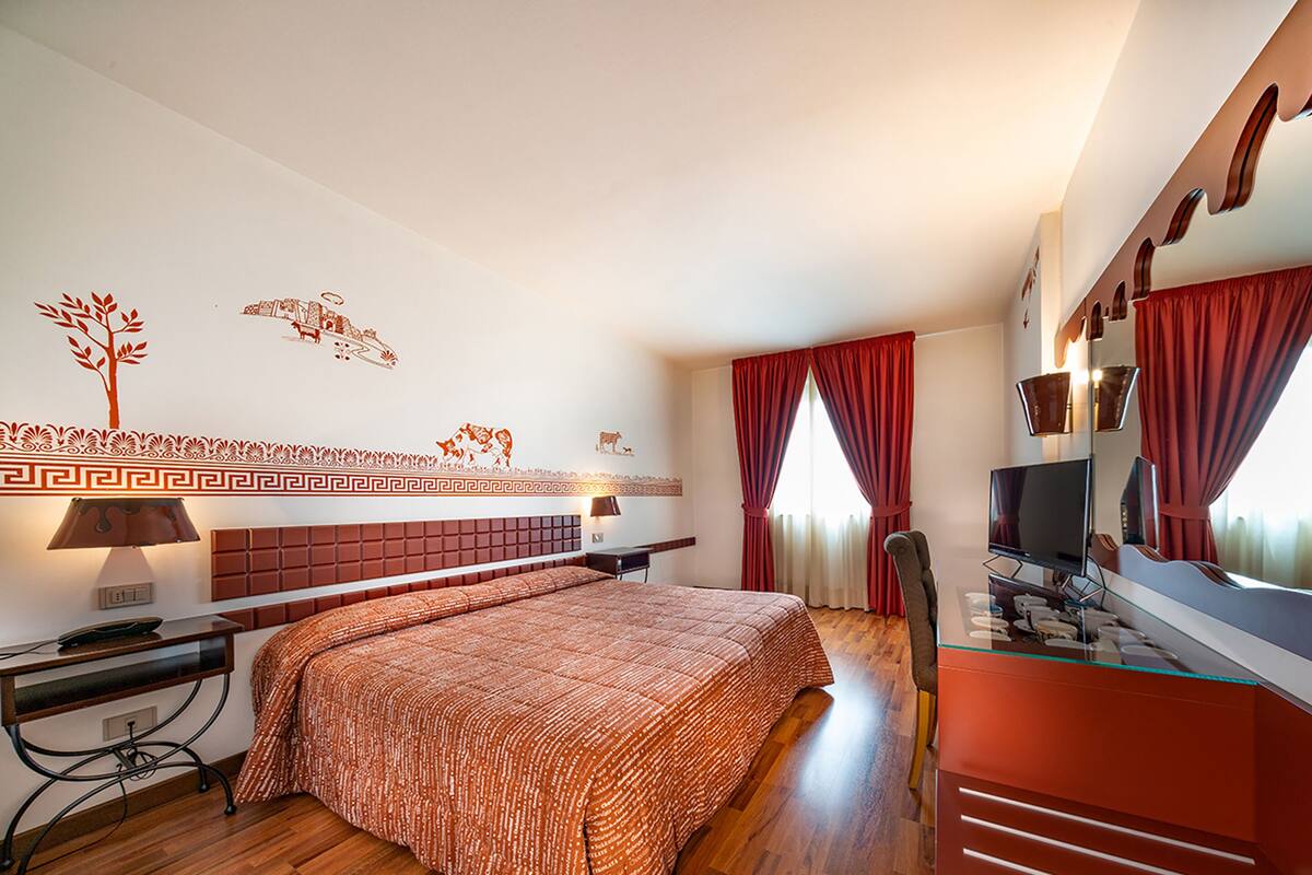 Une chambre d’hôtel moderne dotée d’un grand lit, d’un bureau avec un ordinateur, d’une télévision et d’une salle de bain avec une douche en verre.