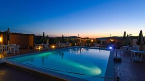 Une piscine entourée d’un mur bas et agrémentée de guirlandes lumineuses, avec des chaises longues et des parasols.