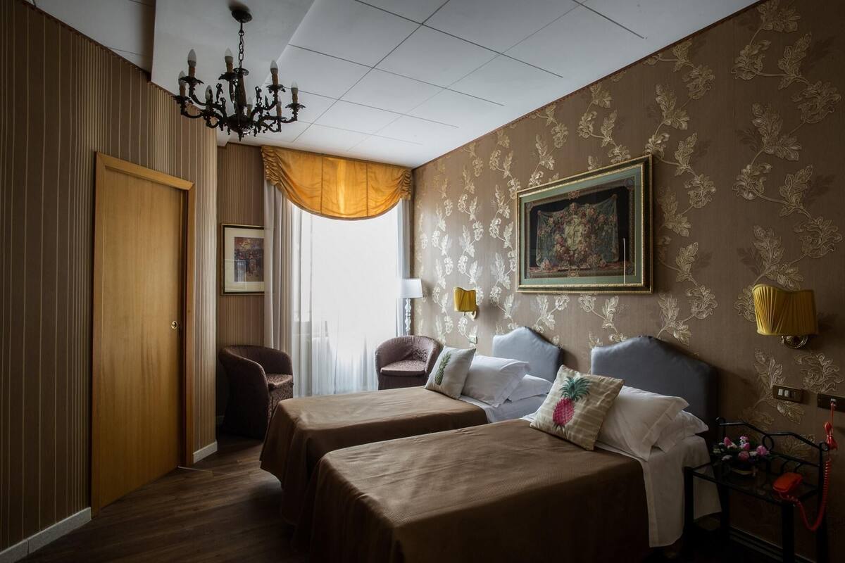 A hotel room with two beds, a chandelier, a painting, and a telephone.