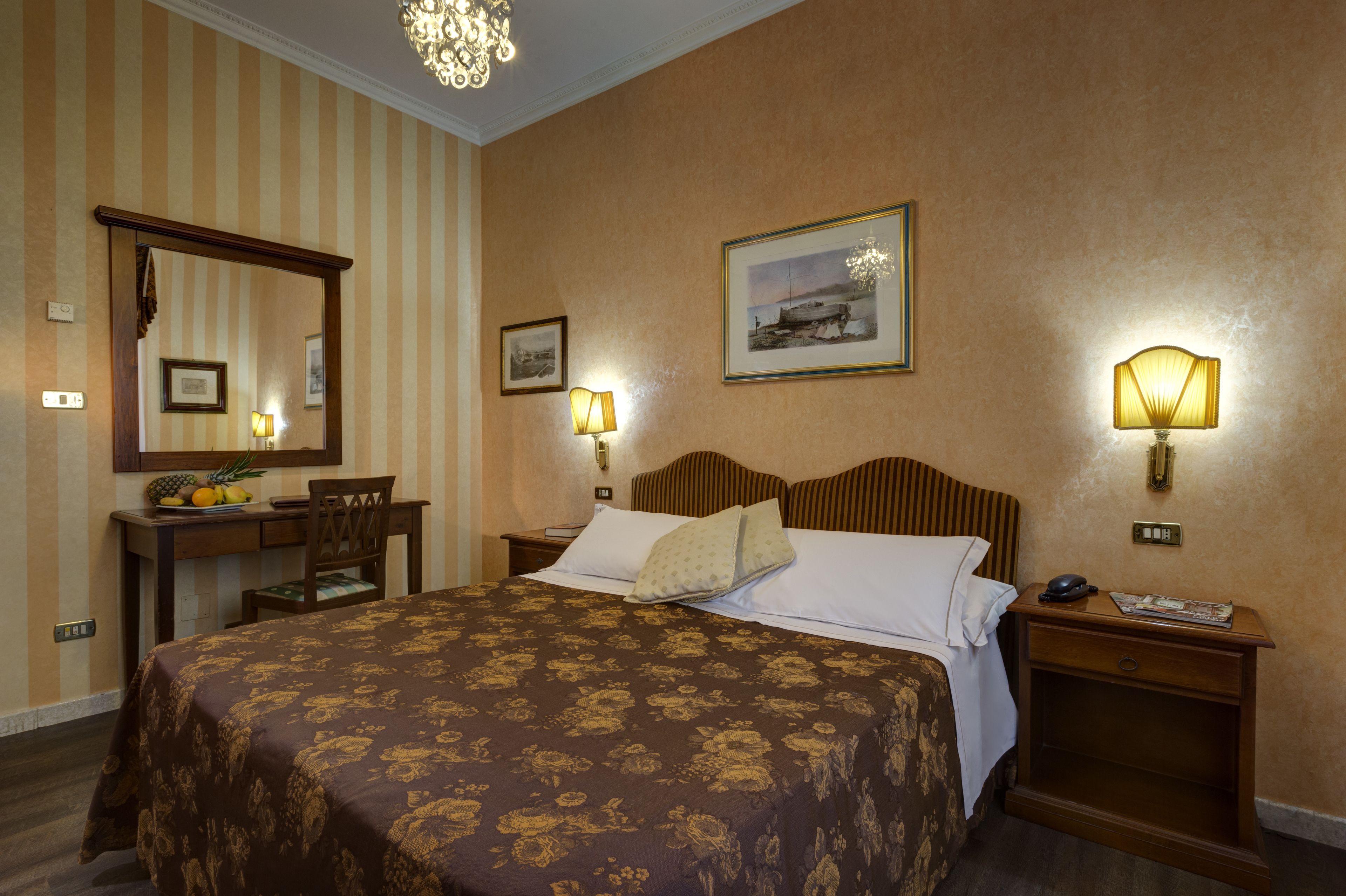 Habitación de hotel con una cama grande, un escritorio con una silla, un espejo y dos lámparas fijadas a la pared.