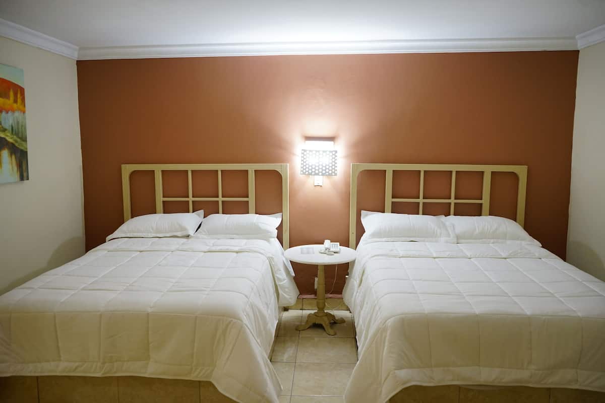 A room with two beds, a small round table, and a wall-mounted light fixture.