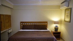 A neatly made bed with a wooden headboard, a bedside lamp, and a nightstand with a phone and a decorative vase. - Hotel Posada del Sol Inn (Torreón)