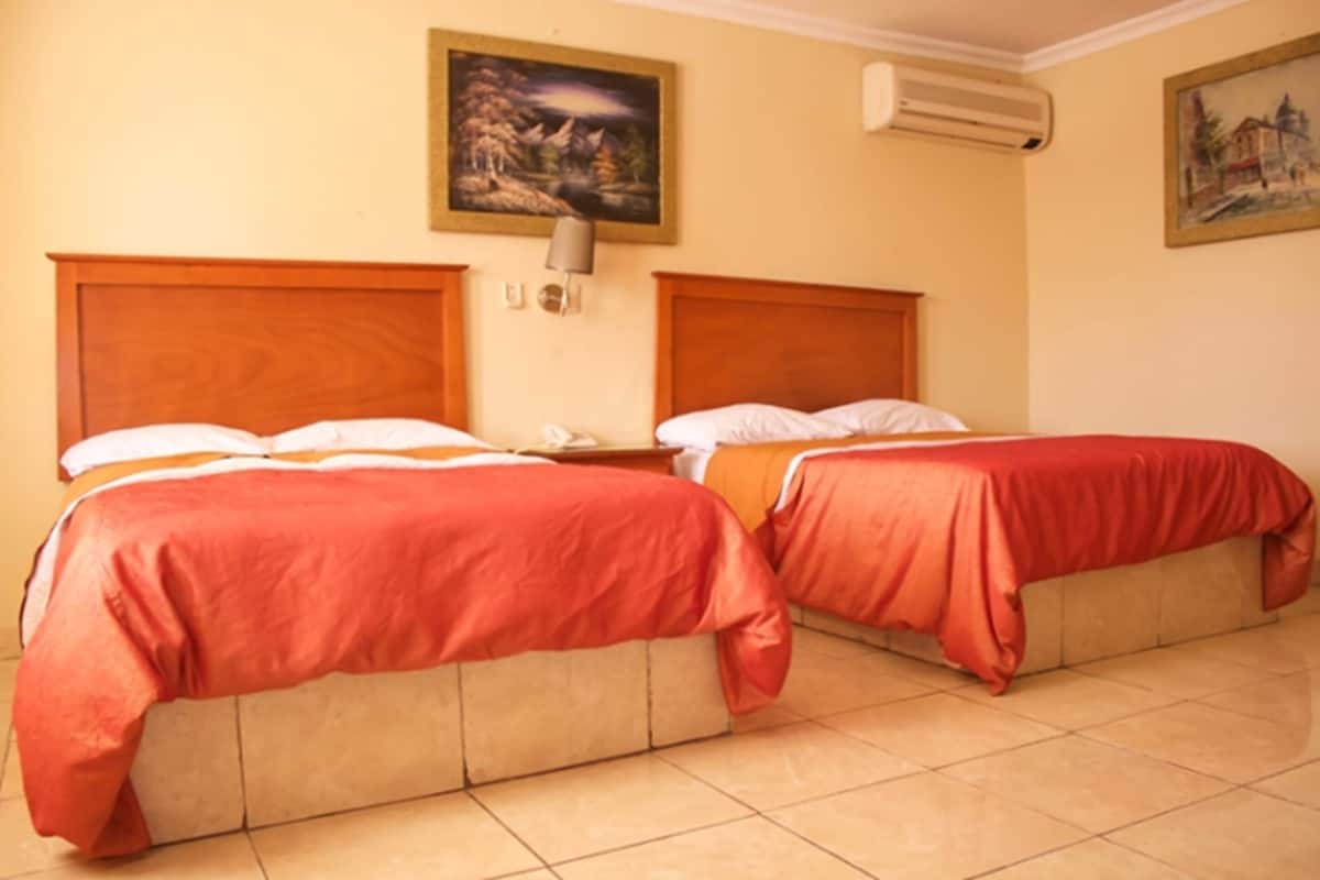 A room with two beds, a nightstand, a lamp, and a painting on the wall.