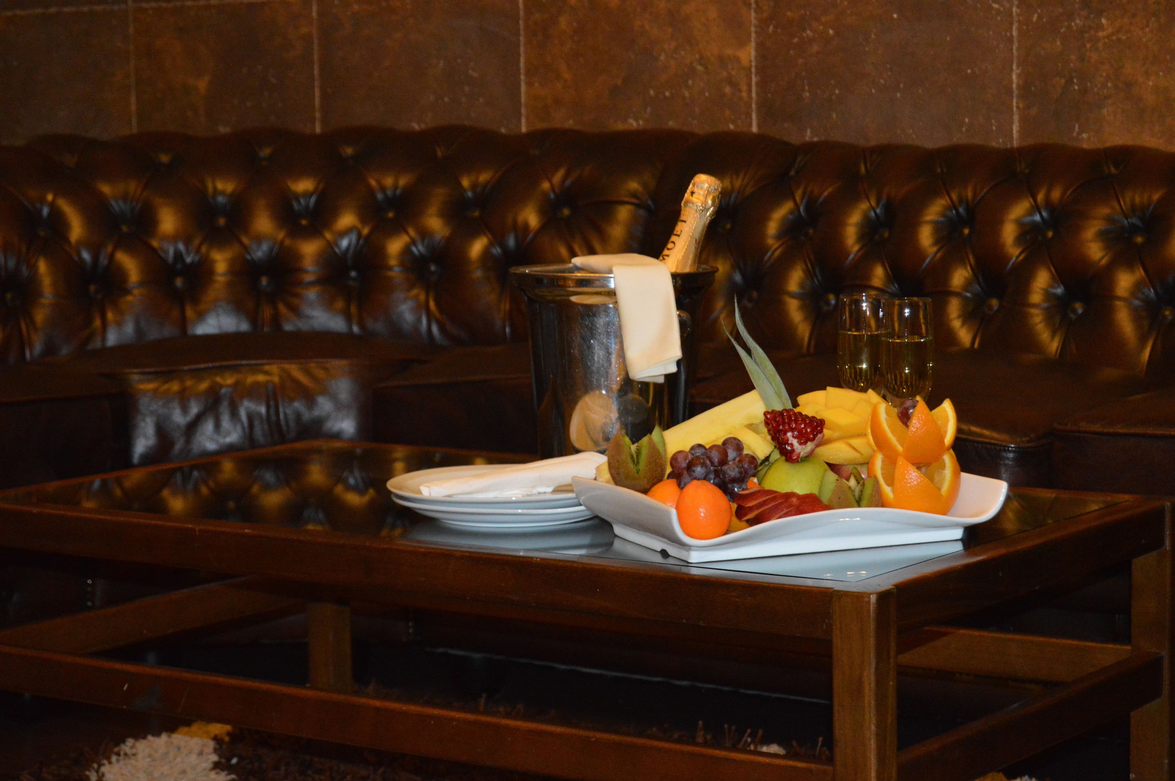 Una mesa de comedor con una bandeja de frutas, champán y copas en una habitación con un sofá de cuero.