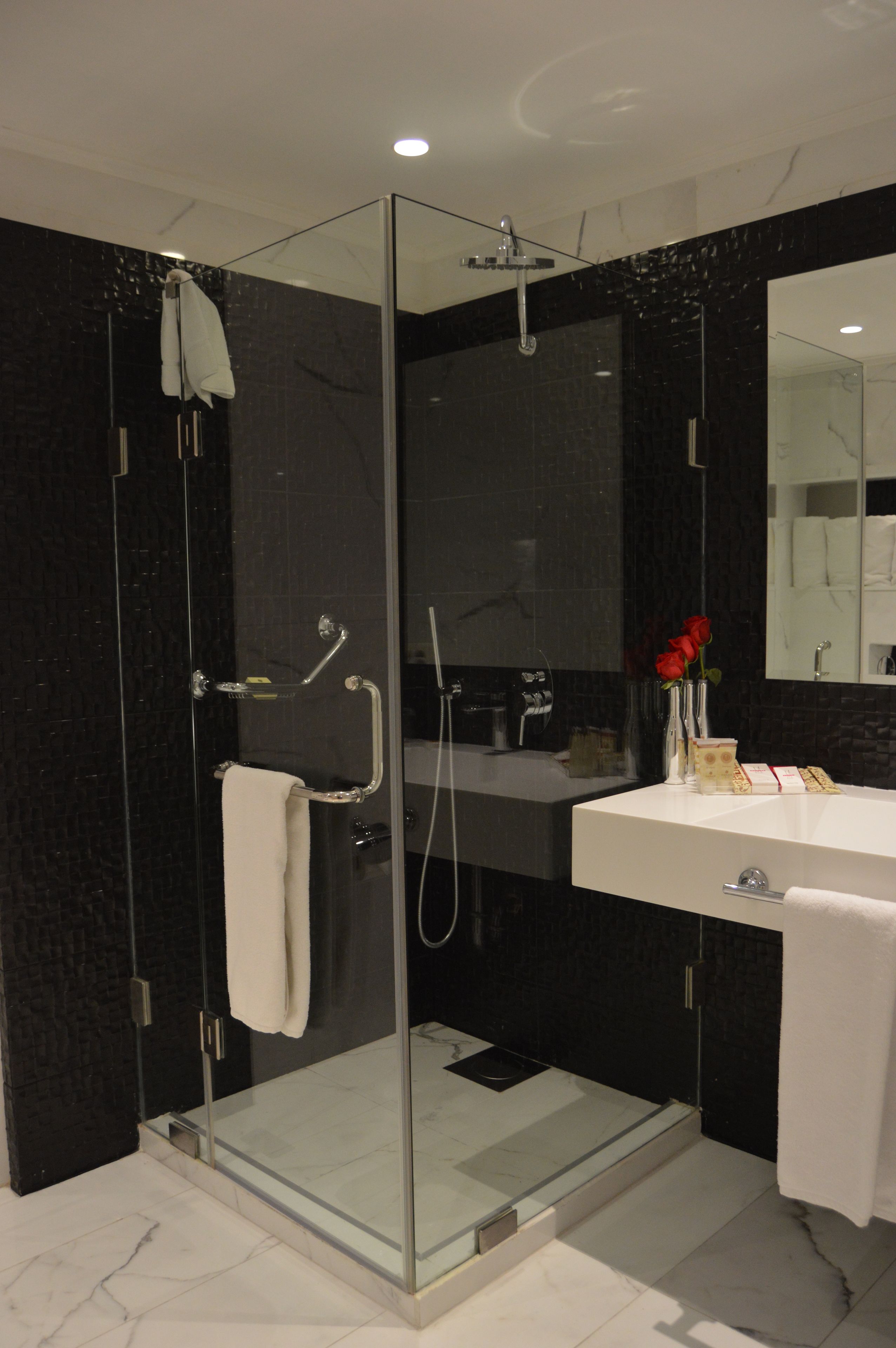 Un baño moderno con ducha de vidrio, lavamanos blanco y un espejo grande.