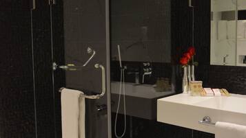 Un baño moderno con ducha de vidrio, lavamanos blanco y un espejo grande.