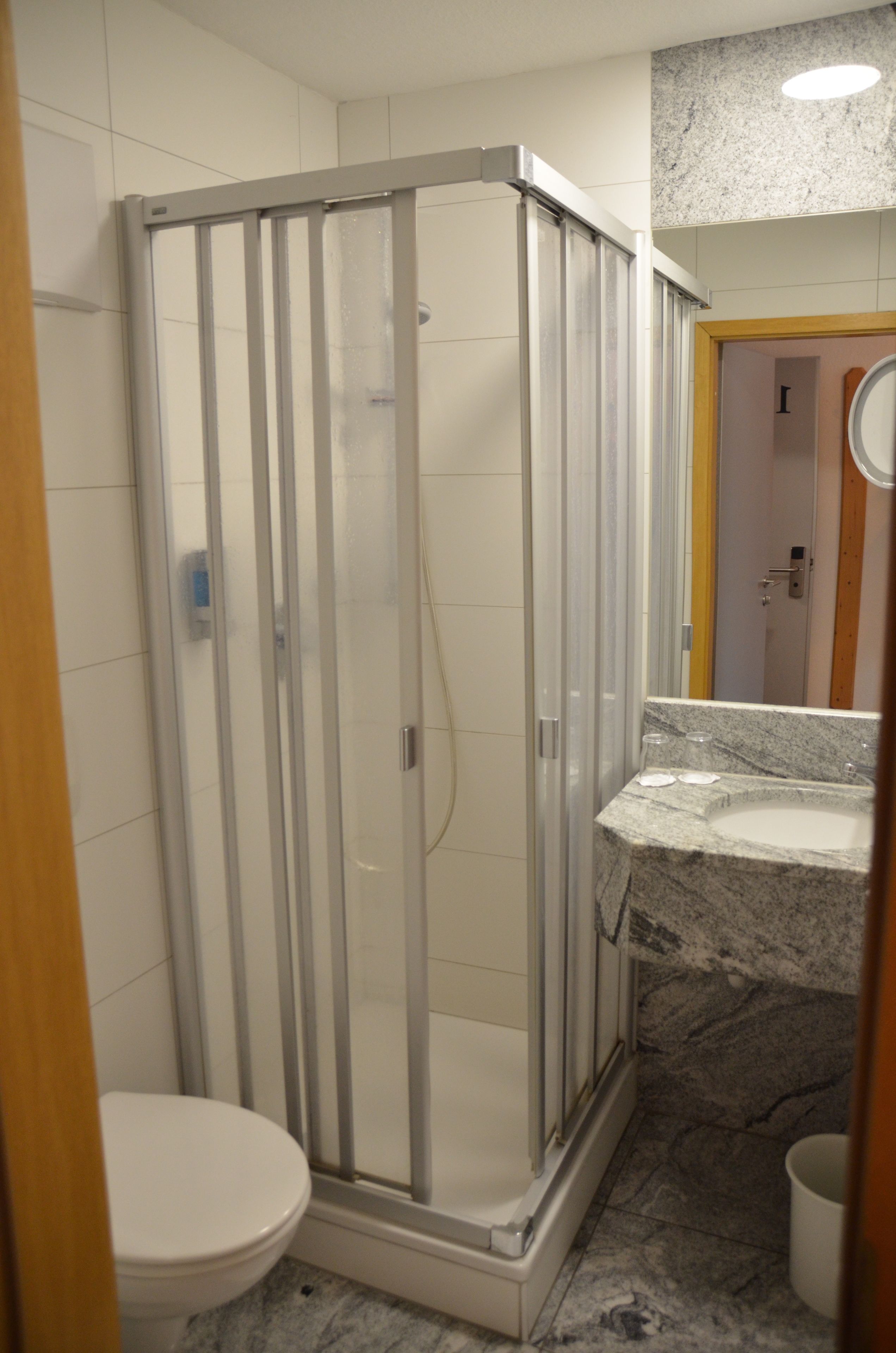 Une salle de bain avec une douche à parois de verre, des toilettes blanches et un lavabo sur un plan de toilette en marbre.