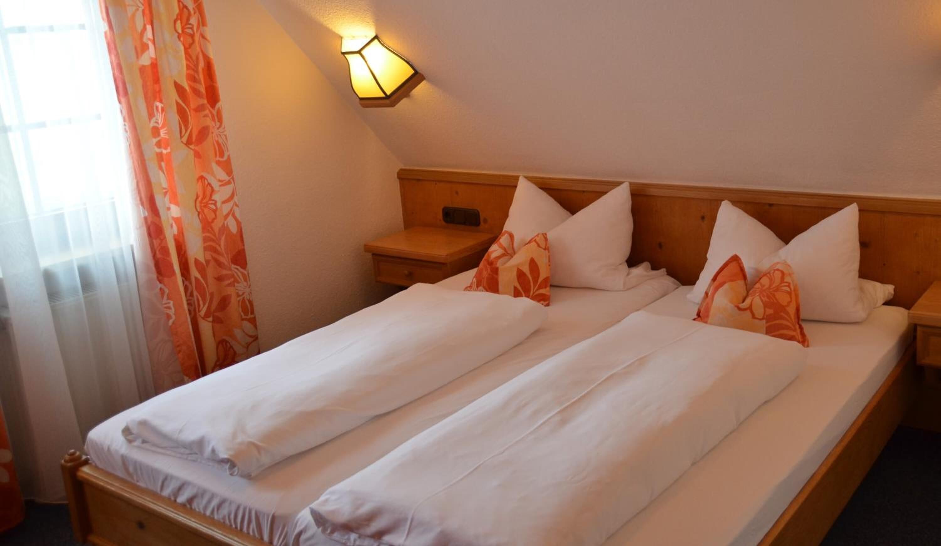 Un lit double avec une literie blanche et des coussins à motifs floraux orange, une tête de lit en bois et une table de chevet avec une lampe.