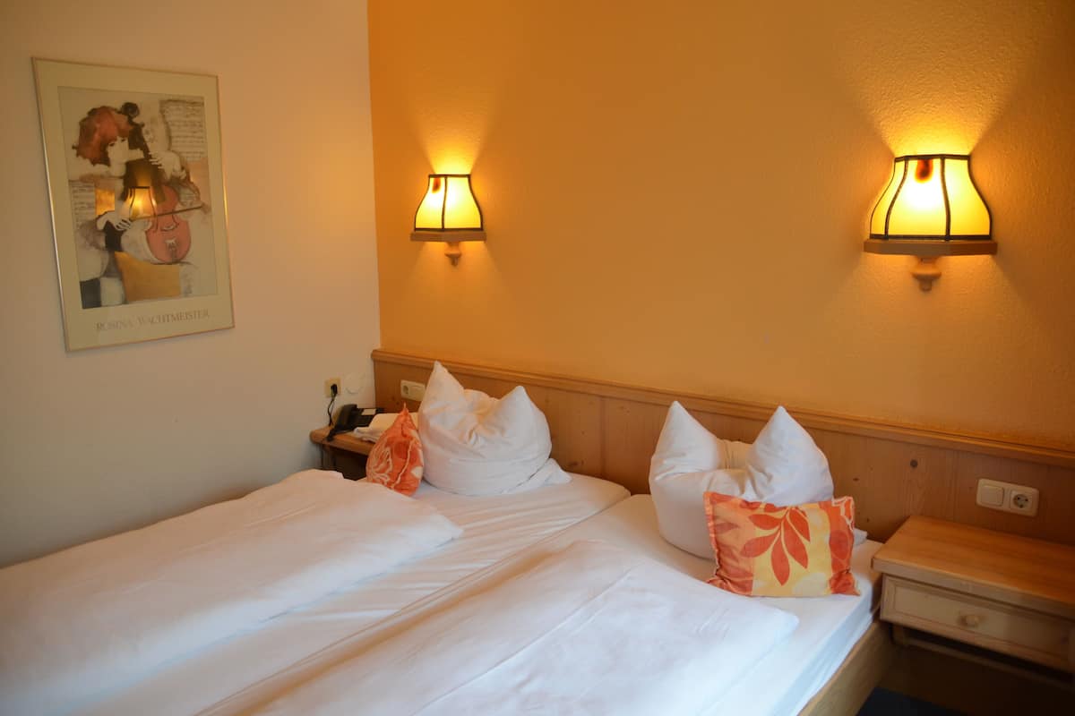 A hotel room with a neatly made bed, two wall-mounted lamps, a framed picture on the wall, and a wooden nightstand with a lamp.