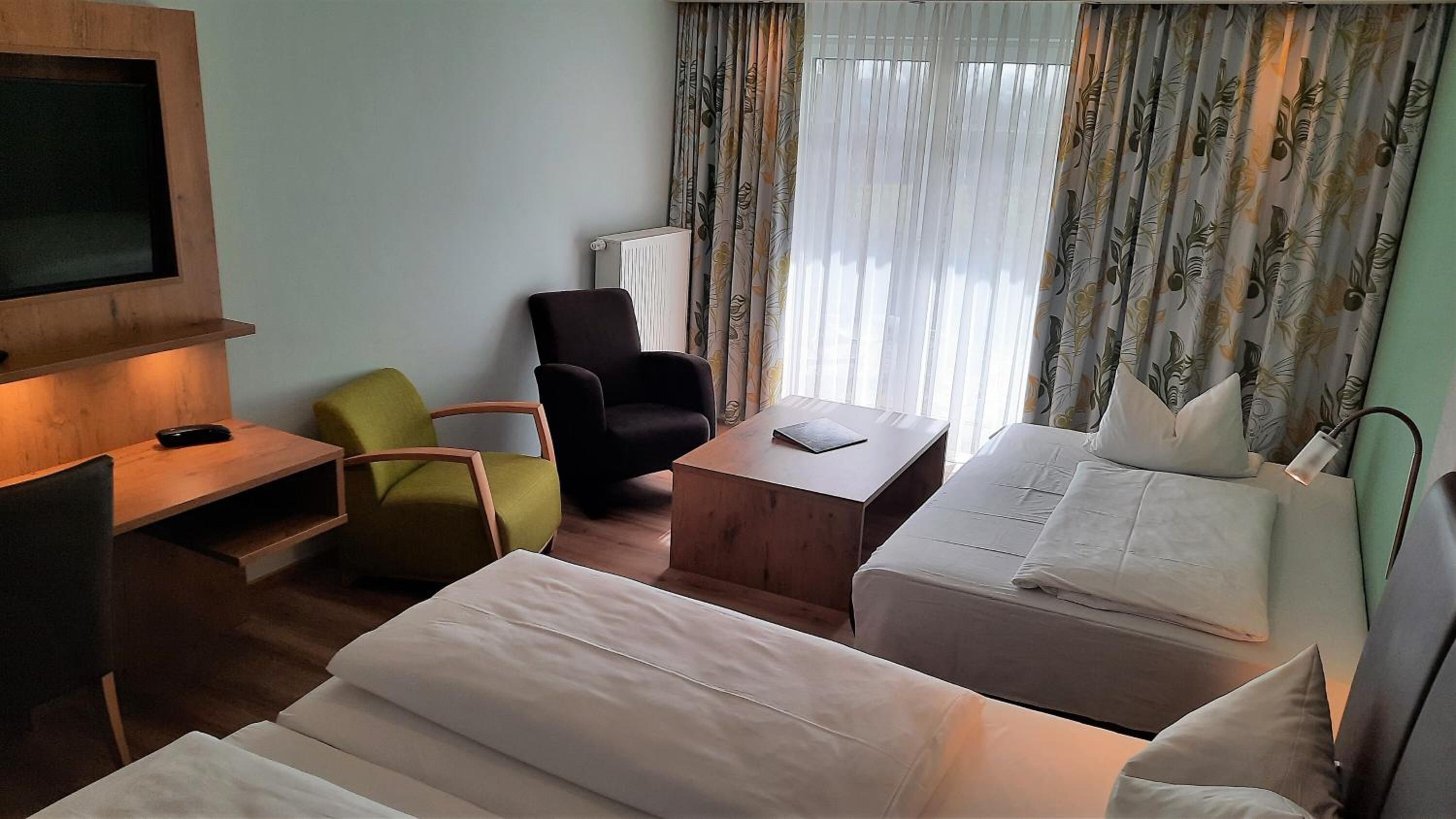 Habitación de hotel con dos camas, un escritorio, una silla, un televisor y una ventana con cortinas.