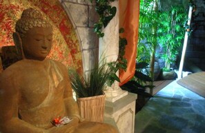 A Buddha statue in a room with a stone wall, a potted plant, and a view of greenery outside. - Hotel Bergwirt (Herrieden)