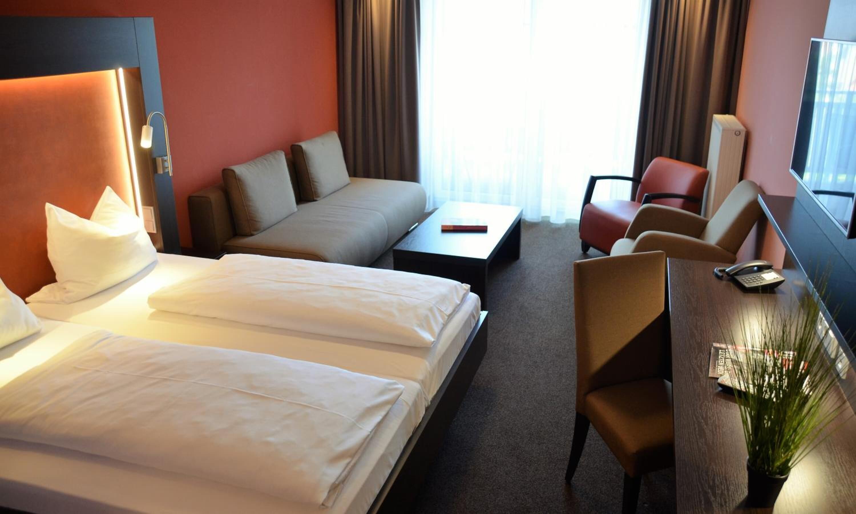 A hotel room with two beds, a sofa, a desk with a telephone, and a chair.