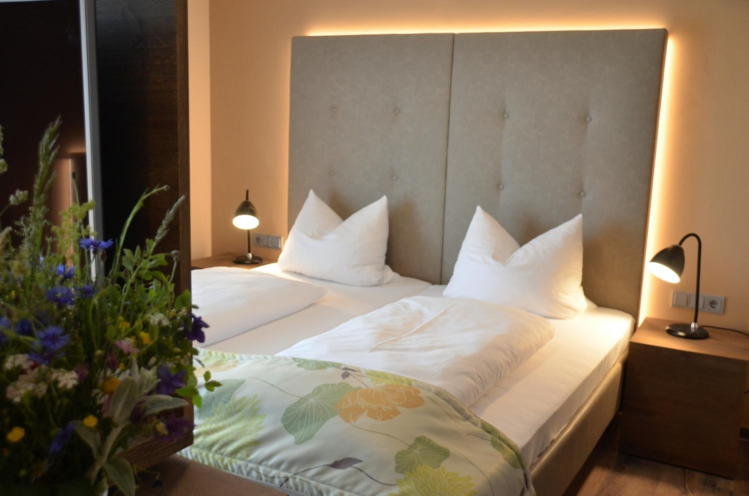 Un lit double avec une tête de lit rembourrée de couleur grise, du linge de lit blanc et deux lampes de chevet.