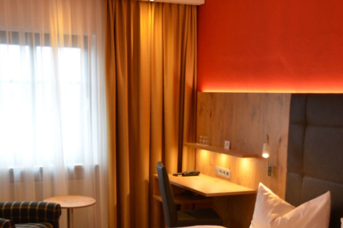 A hotel room with a bed, a desk, a chair, and a small table.