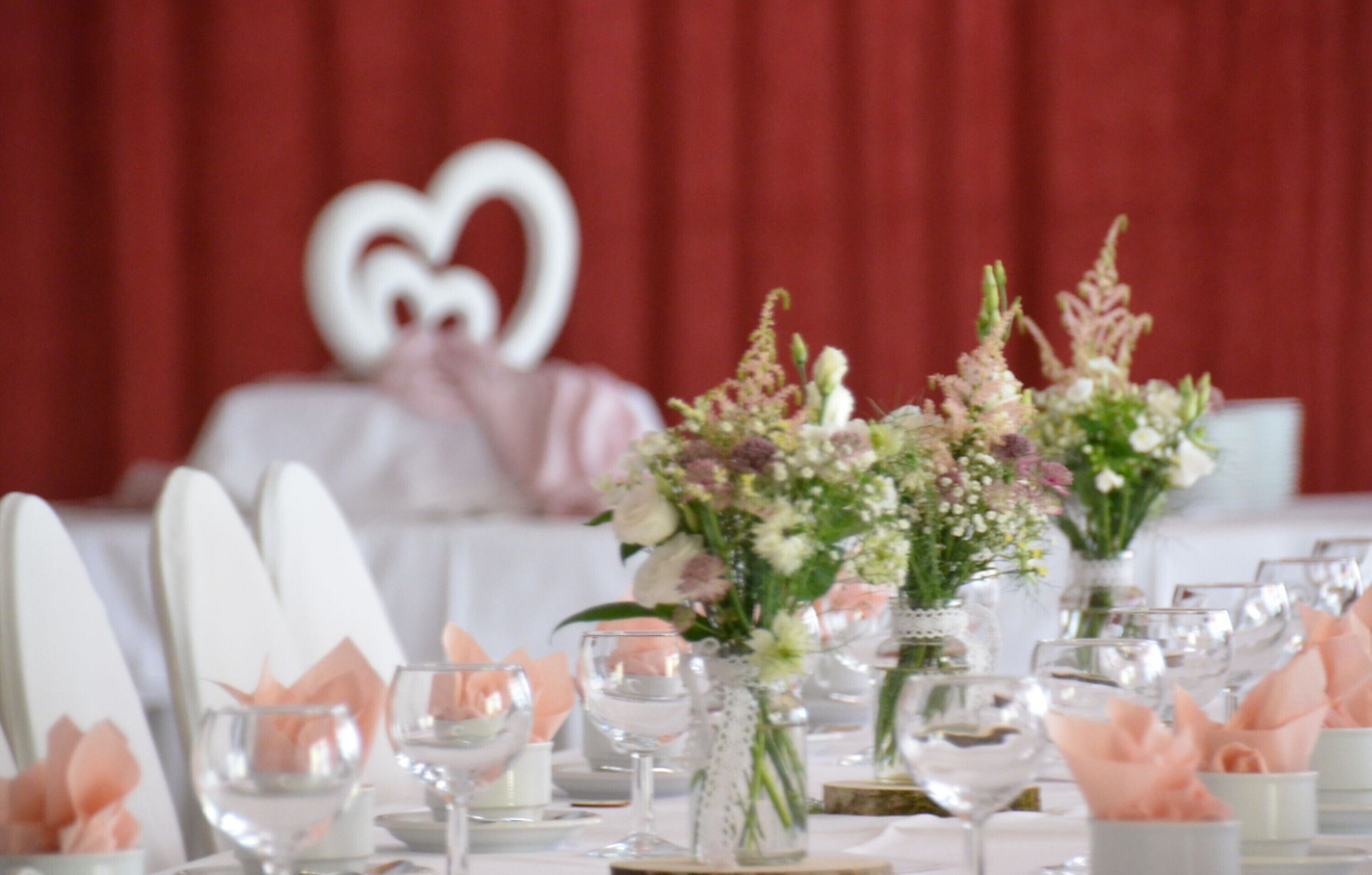 A table set for a formal event with white chairs, glassware, and floral centerpieces.