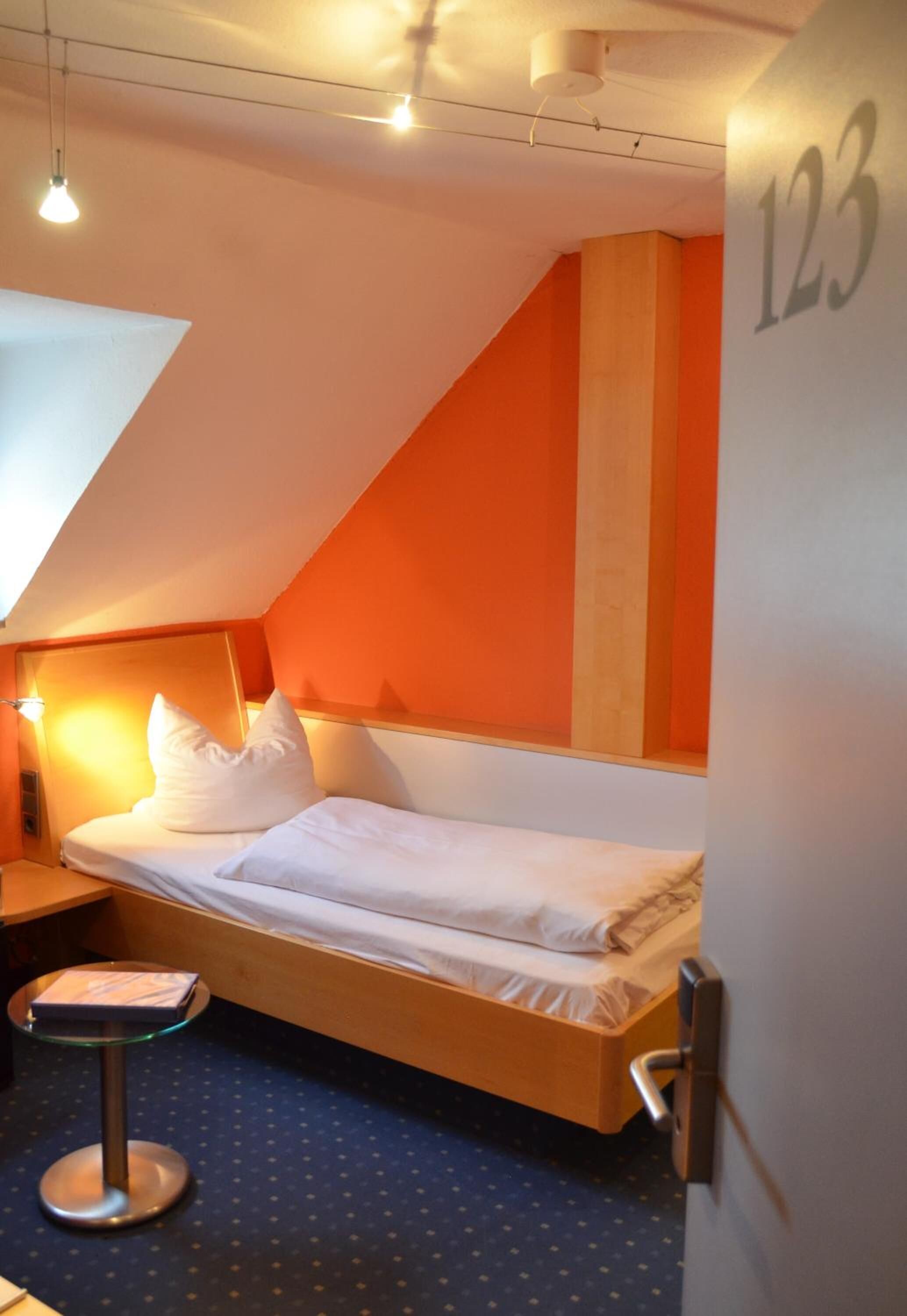 A single bed in a room with a sloped ceiling, a small round table, and a door with the number 123.