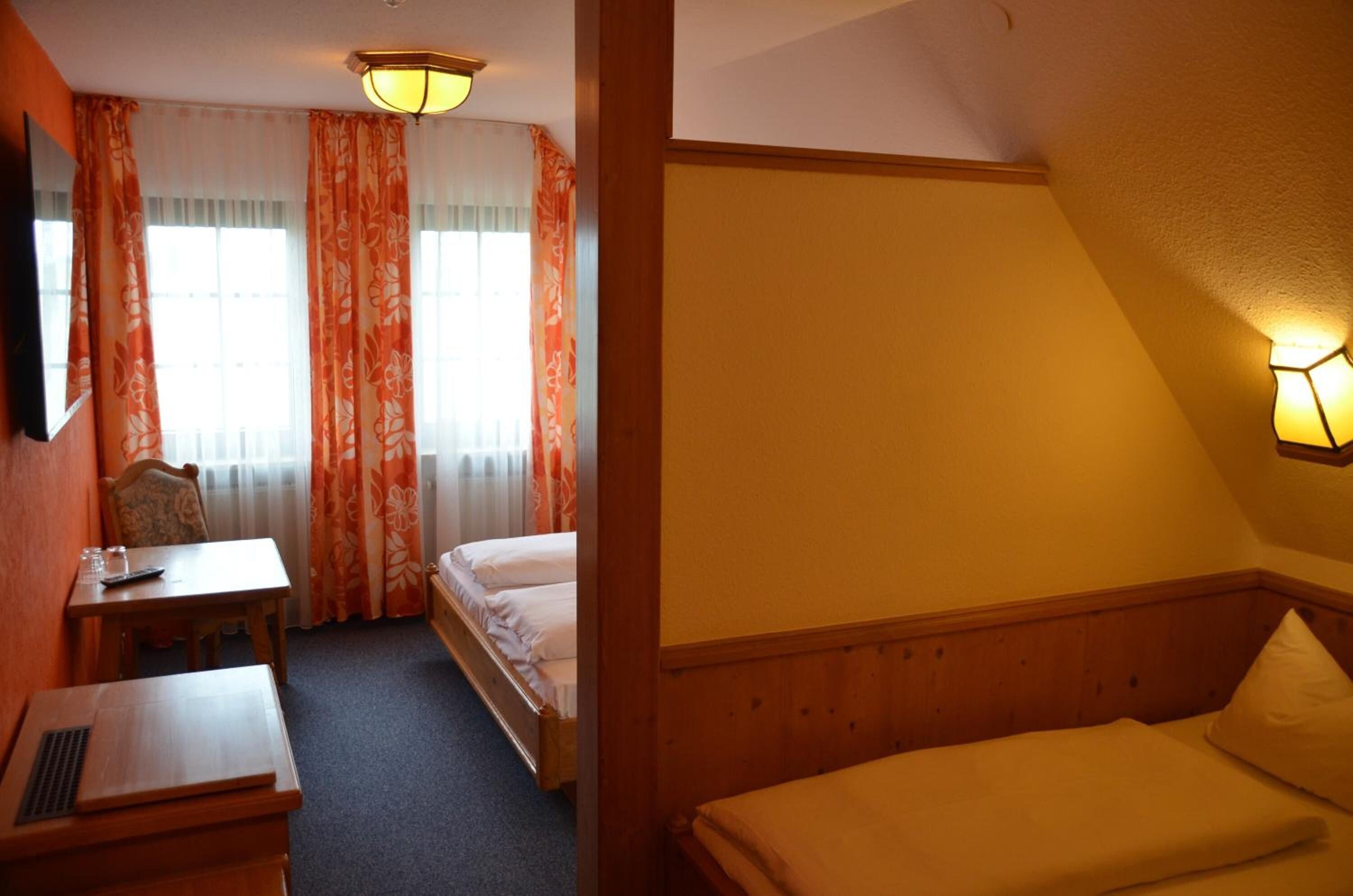 Habitación de hotel con cama, escritorio, silla y ventana con cortinas.