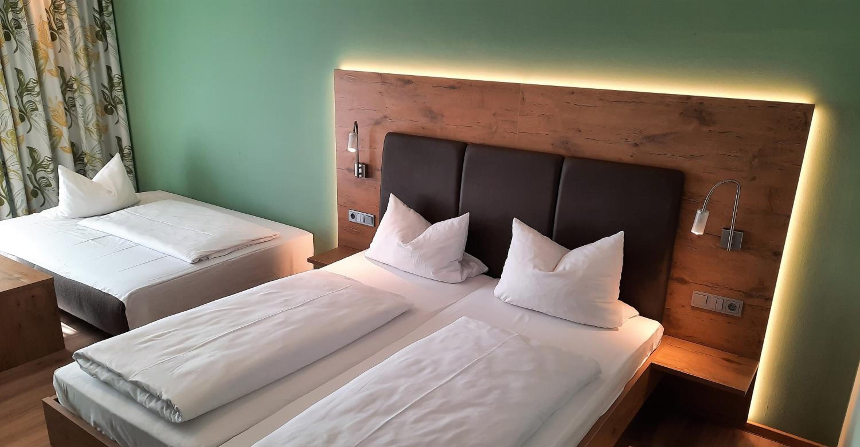 Two single beds with wooden headboards and white bedding, a nightstand with a lamp, and a green wall.