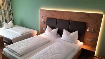 Two single beds with wooden headboards and white bedding, a nightstand with a lamp, and a green wall.
