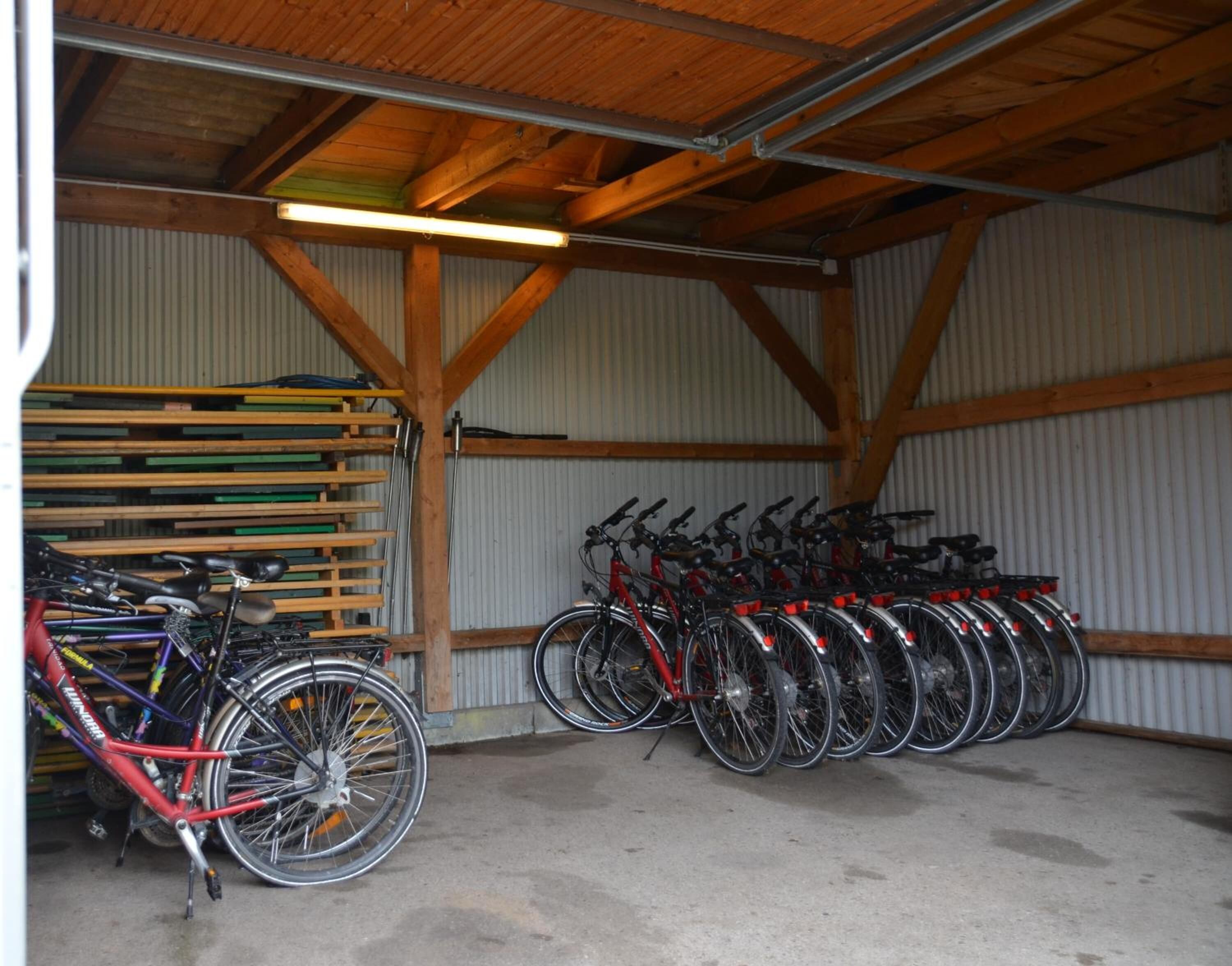 Espaço de estacionamento para bicicletas coberto, com vigas de madeira e paredes de chapa ondulada.